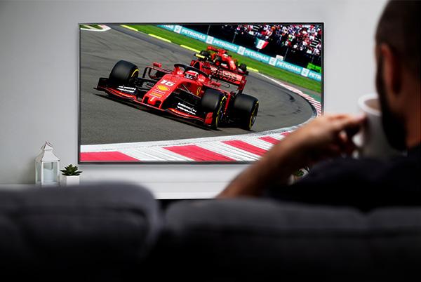 a man sitting on couch watching a formula one race on tv