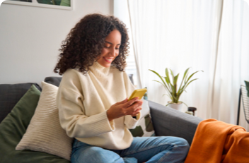 A woman sitting on a sofa looking at a smart phone and smiling