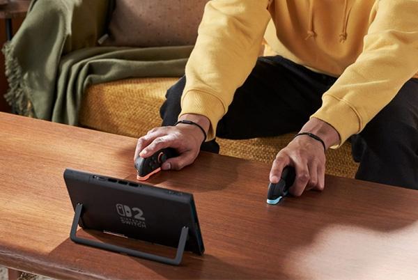 a man sitting on a couch playing a nintendo switch 2 on a coffee table with the joy con controllers in mouse mode