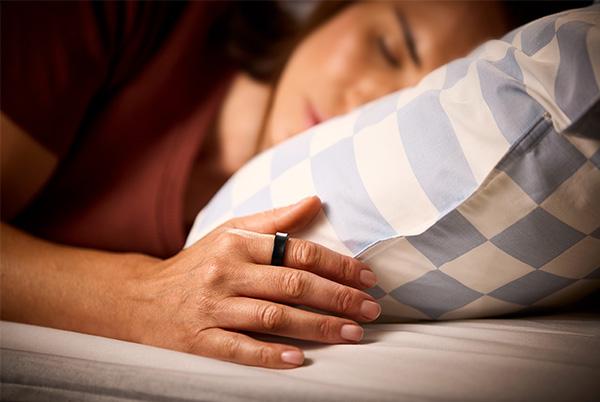 a woman sleeping in a bed wearing a samsung galaxy ring with her hand resting next to a pillow