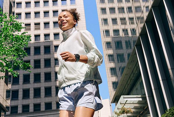 a woman in a white shirt and shorts running in a city wearing a samsung galaxy watch 7