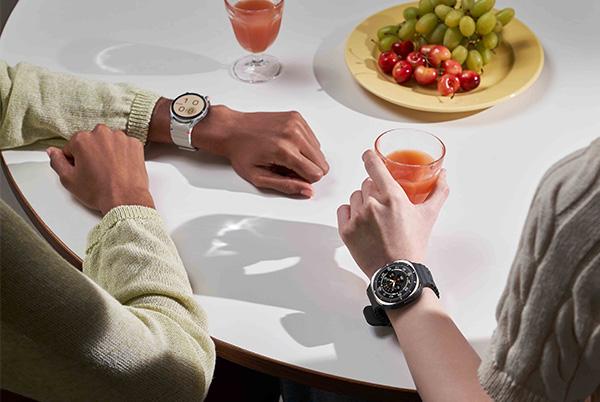 two people sitting at a table with drinks and fruit wearing samsung galaxy watch 7 smart watches on their wrists
