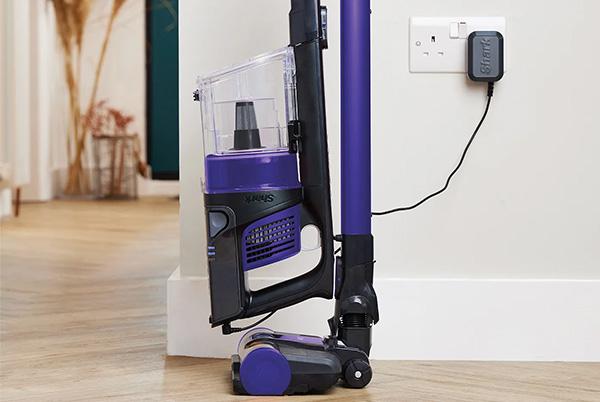 a purple and black shark vacuum cleaner sitting on a floor charging