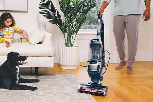 a person cleaning their floor with a vacuum with a dog and child sitting next to them