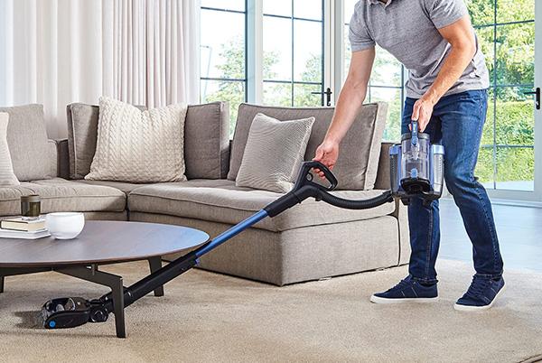 a man vacuuming under a living room coffee table with a shark cordless vacuum