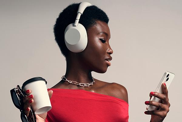 a woman in red wearing sony white headphones while holding a coffee cup and phone