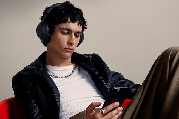a man in a leather jacket sitting on a red chair wearing sony wh-1000xm6 headphones