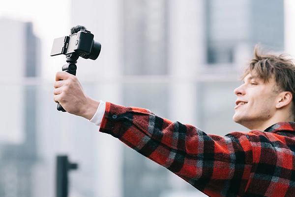 a man holding a camera up to his face while standing in front of a city