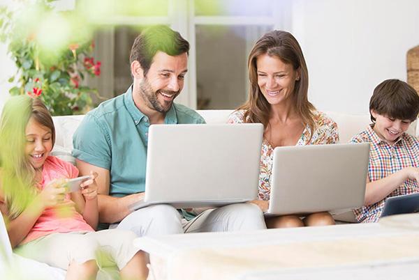 a family sitting on a couch with laptops in front of them