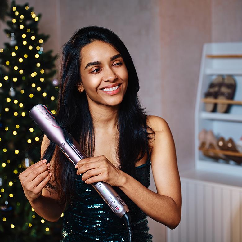 a woman in a green dress holding a Shark hair styler in front of a christmas tree