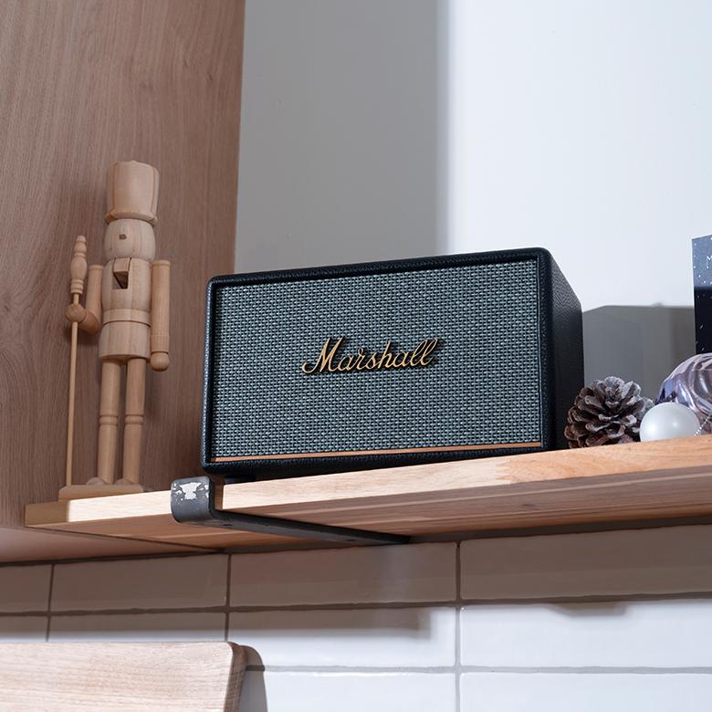 a Marshall Bluetooth speaker sitting on a shelf next to a wooden figurine