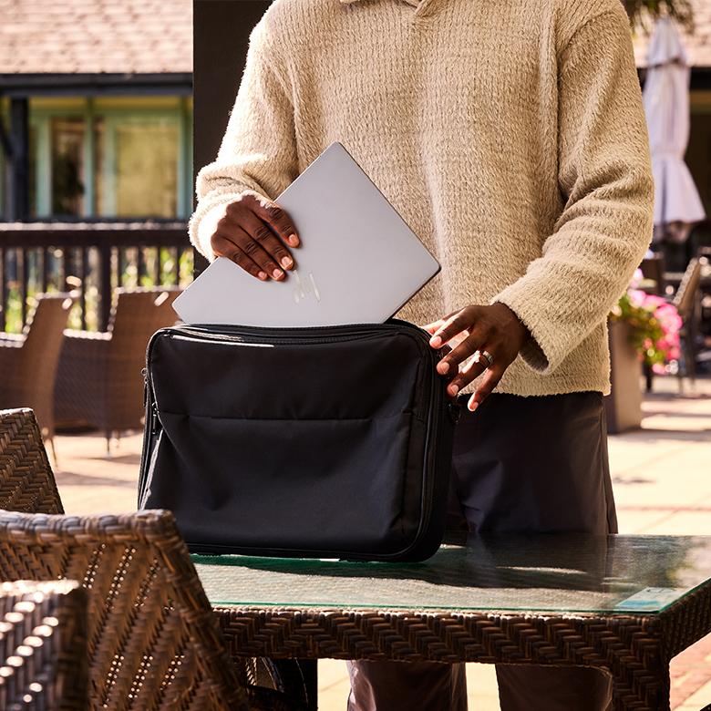 a man holding a laptop bag and a laptop on a table