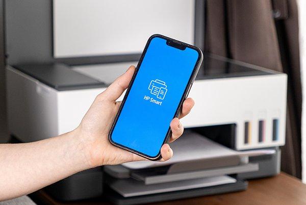 A person holding a phone with the HP Smart app displayed on-screen.