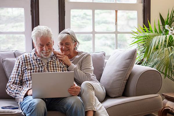 an older couple sitting on a couch looking at a Windows laptop