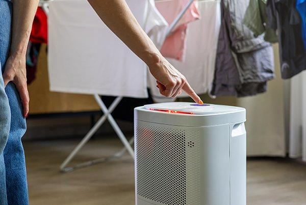 a person pointing at a small white air conditioner in a laundry room