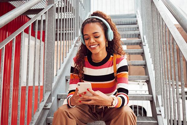 a woman sitting on some stairs with headphones on and a cell phone