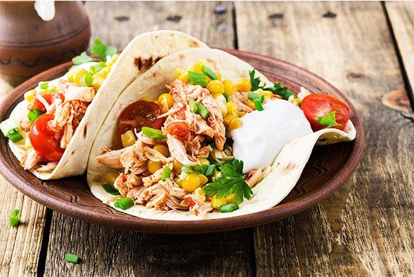 a plate of tacos with chicken and vegetables on a wooden table