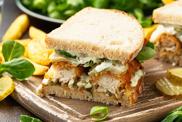 A fish finger sandwich cut in half on a wooden cutting board