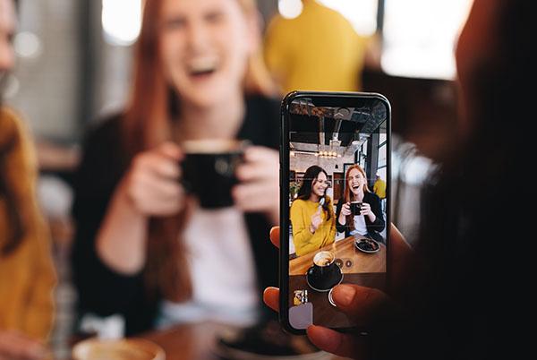A woman taking a picture of three people in a cafe on their iPhone.