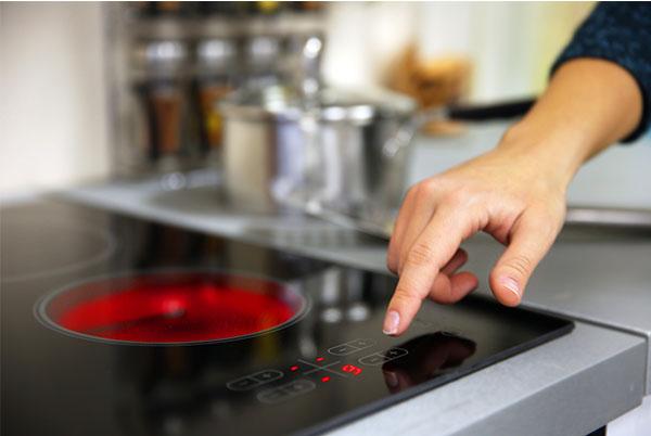 a person touching a button on an induction hob with a red pot on it