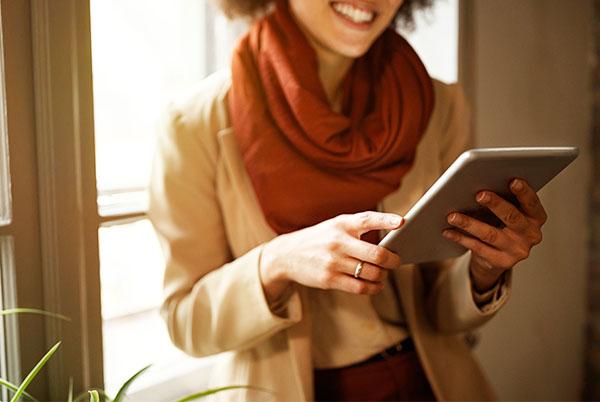a woman smiling while holding a tablet computer in front of a window