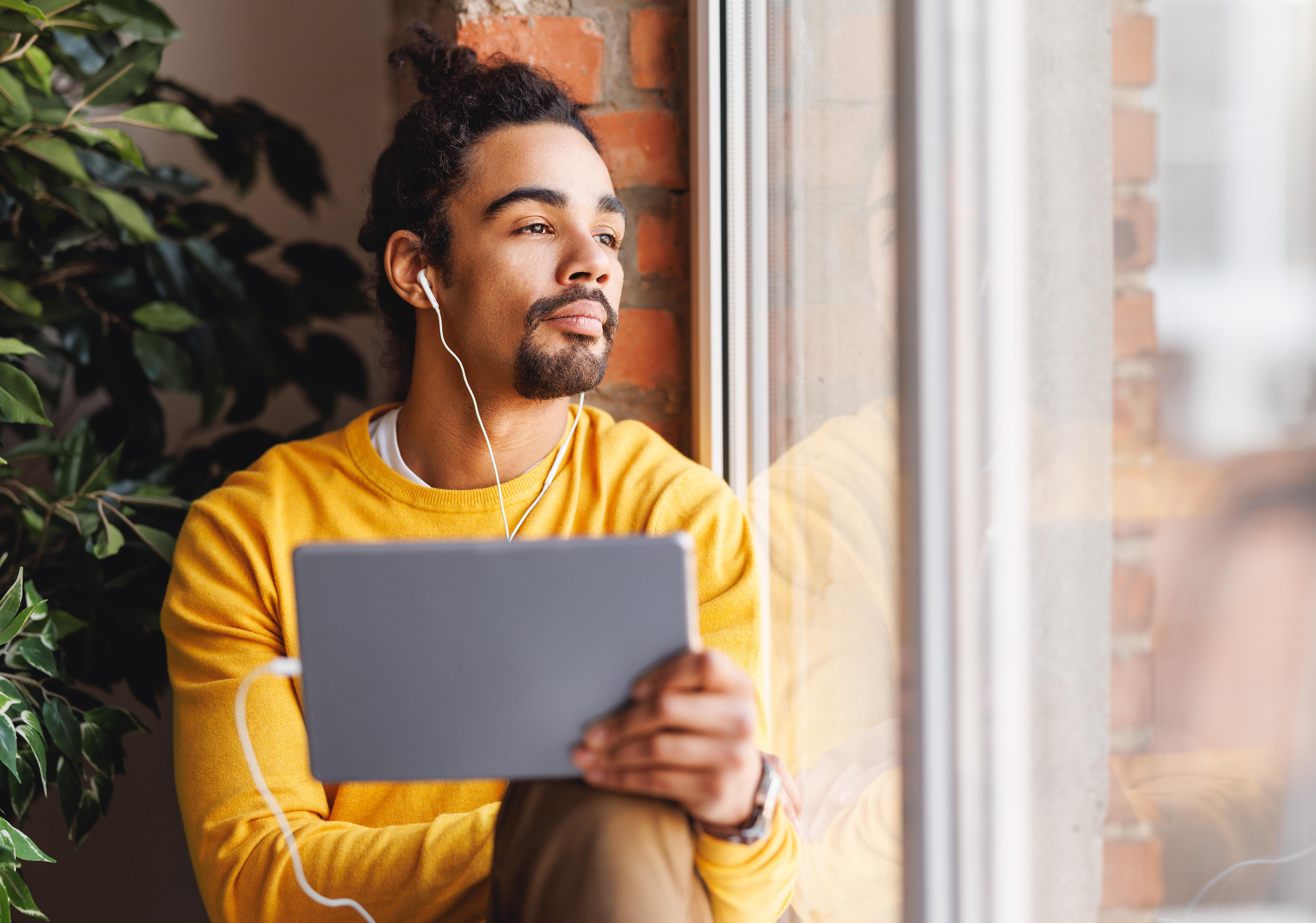 a man with headphones and a tablet sitting on a window sill