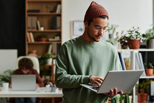 a man in a beanie and sweater using a laptop