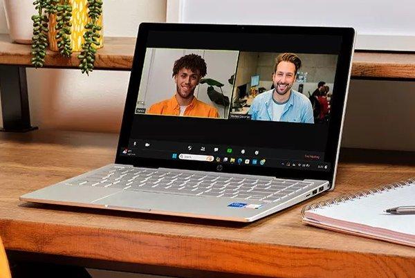 a laptop computer sitting on a wooden desk with a pen and paper