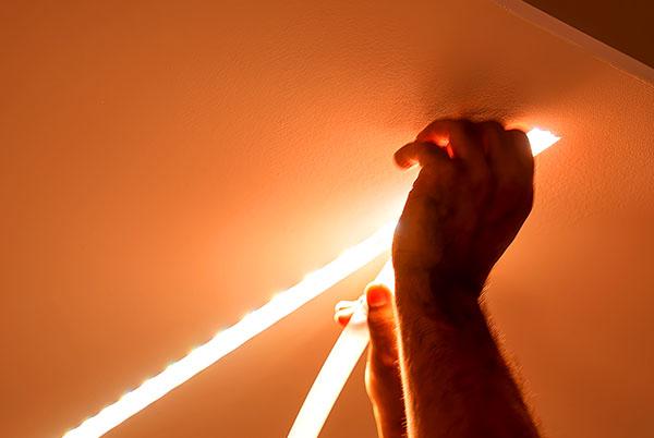 a person holding a light strip in the air while working on a ceiling