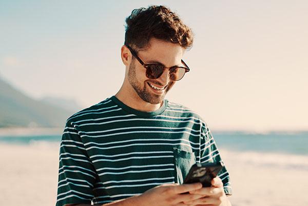 a man in sunglasses and a striped shirt is smiling while looking at his phone