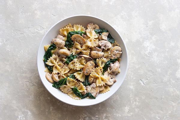 a bowl of pasta with mushrooms and spinach in it
