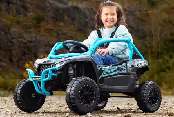 a young girl riding a toy atv on a gravel road