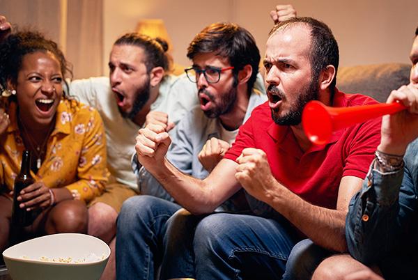 a group of people sitting on a couch watching football on TV