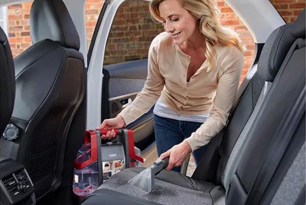 a woman cleaning the back seat of a car with a vacuum