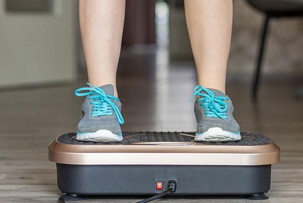 a woman standing on a vibrarion plate in blue training shoes