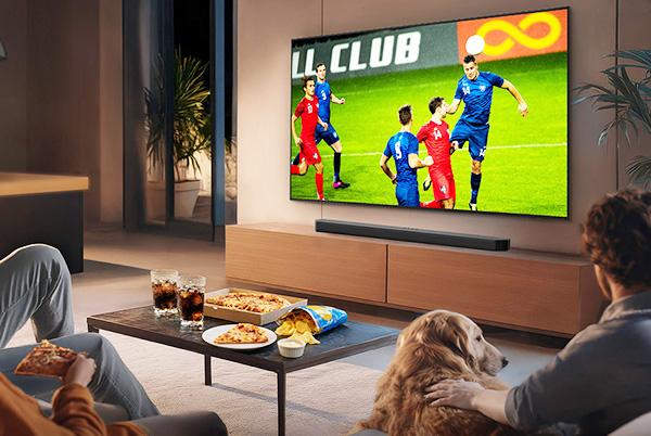 a group of people sitting in a living room watching a soccer game on a television