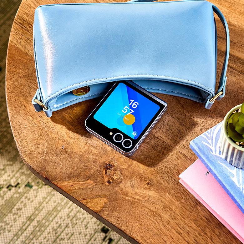 a blue purse sitting on top of a wooden table next to a samsung galaxy flip6 phone