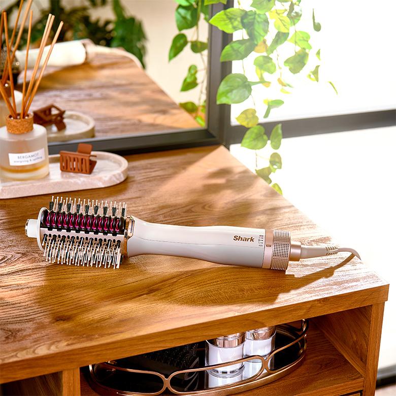 a shark smoothstyle hot air hair styler sitting on a wooden table next to a mirror