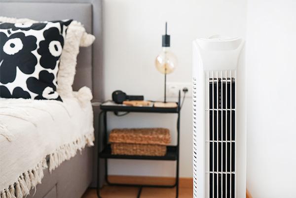 a white tower fan in a bedroom next to a bed and table