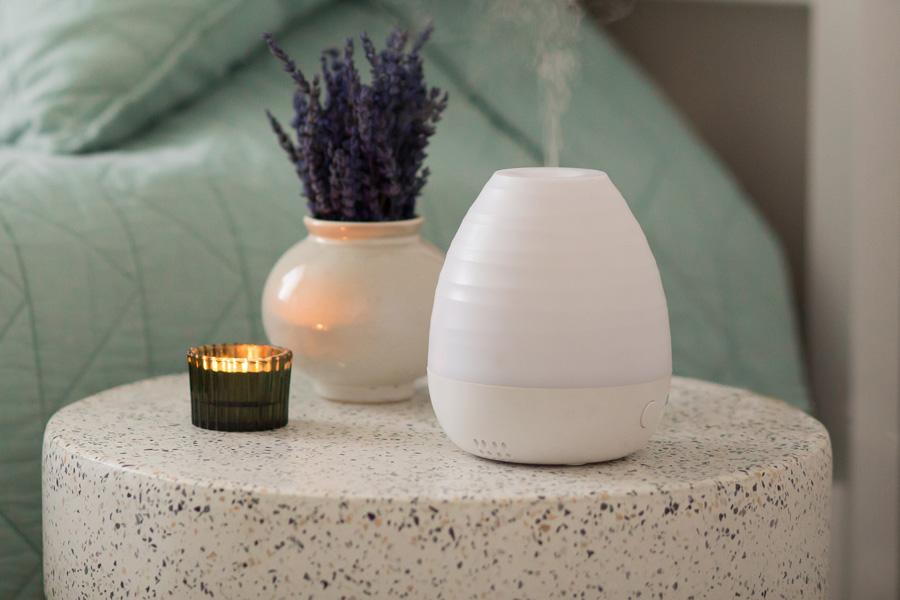 a purple flower and a bottle of essential oil on a table with an electric diffuser