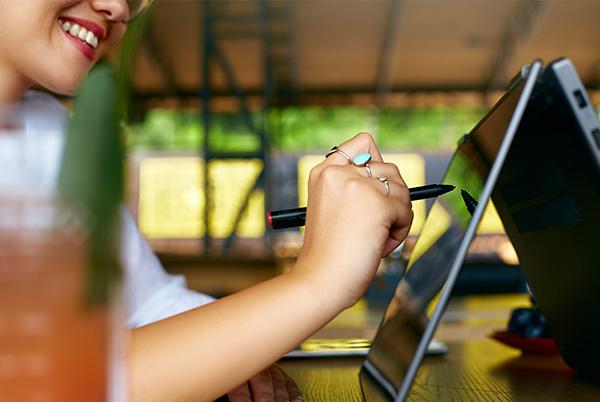 a woman sitting at a table with a 2 in 1 laptop and a pen