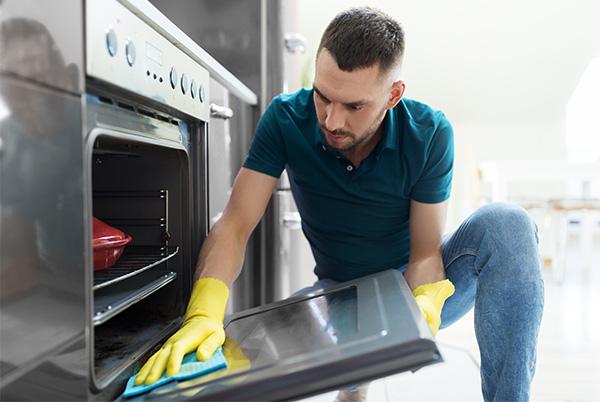 a man in yellow gloves cleaning an oven with a sponge