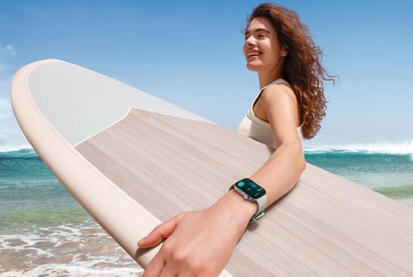 a woman holding a surfboard on the beach wearing a huawei smart watch