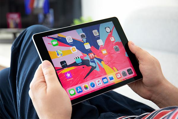 a person sitting on a couch holding an ipad with colourful app icons on the screen