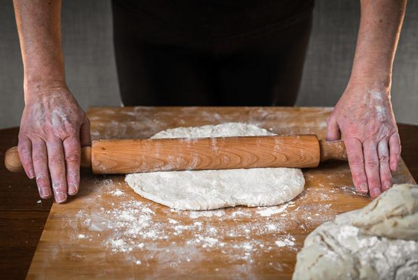 a person rolling out dough on a wooden board with a rolling pin