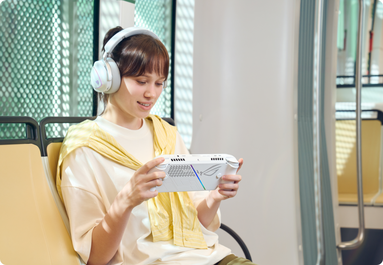 a woman sitting on a sofa with headphones on looking at a handheld gaming console