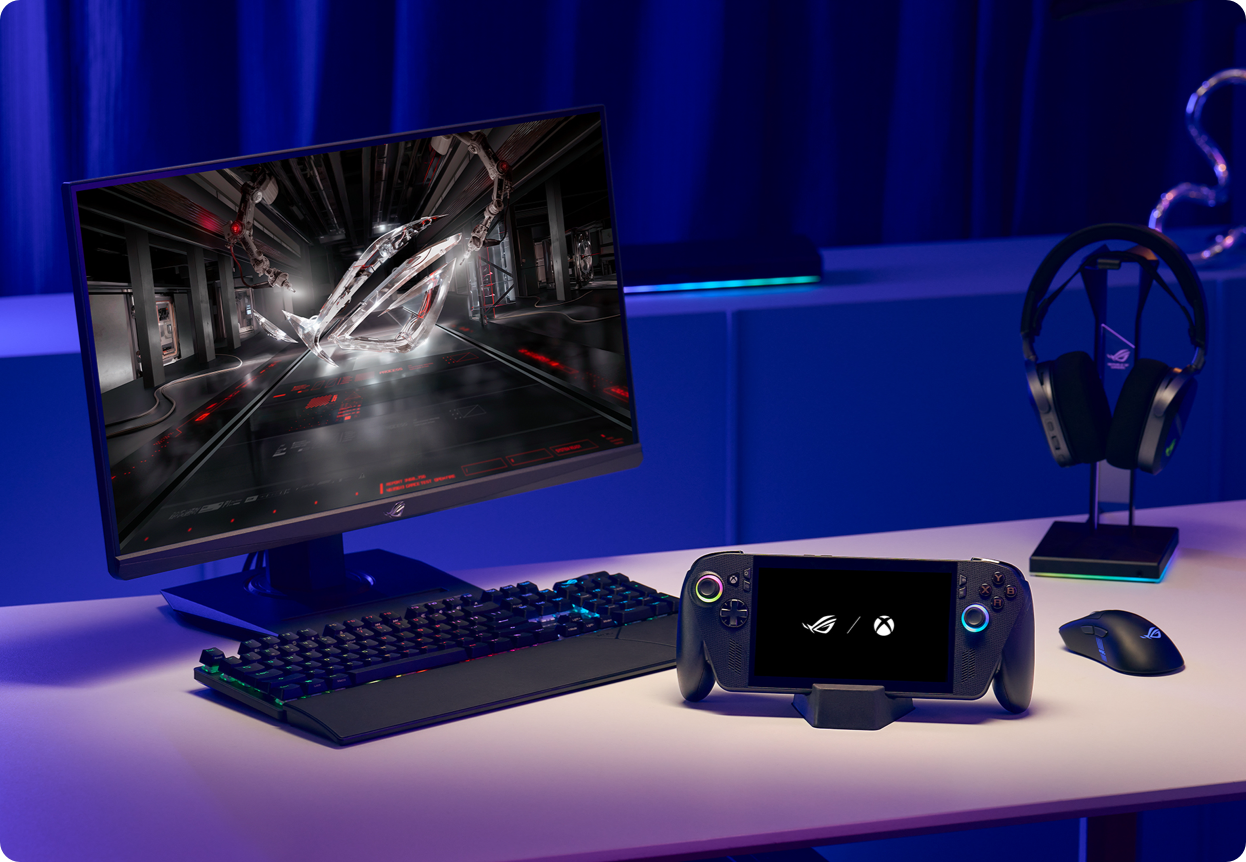 a handheld gaming console, computer monitor, keyboard, mouse and headset on a desk 