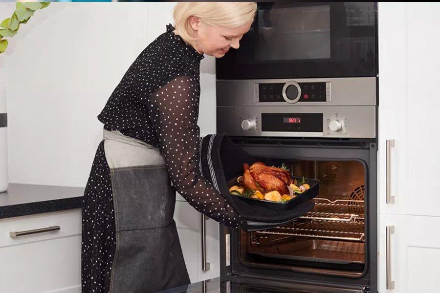 A woman wearing oven gloves taking a roast out of the built-in oven