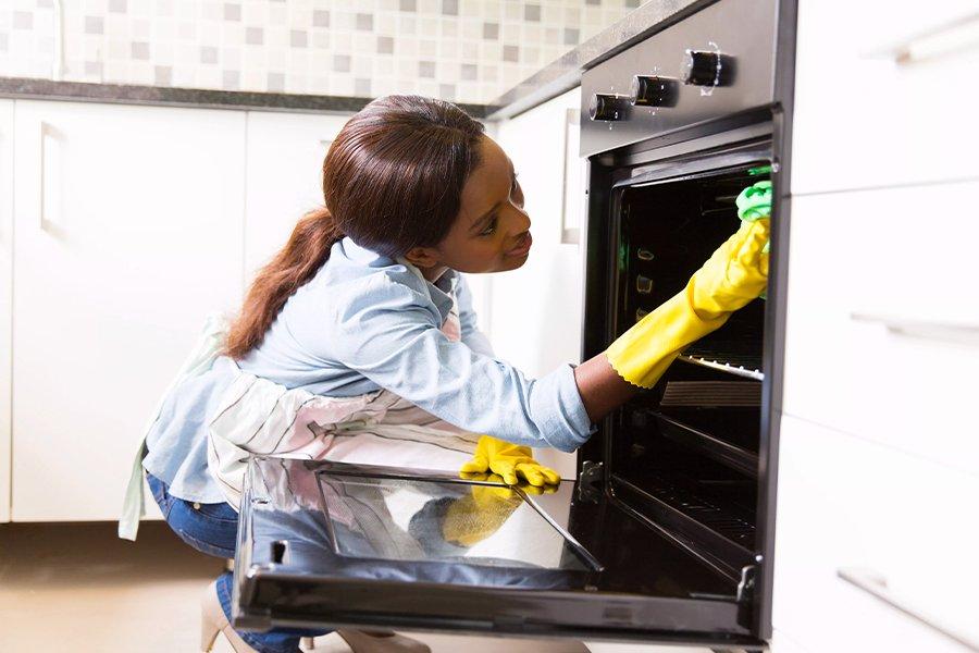 A woman wearing rubber gloves cleaning a built-in oven