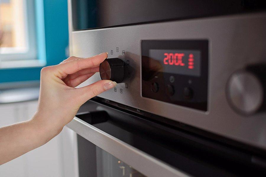 A hand changing the temperature on a built-in oven